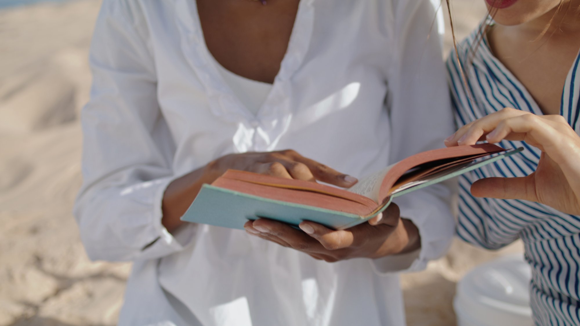 closeup-hands-open-book-pointing-page-beach-picnic-relaxed-girls-read-romance-in-summe-SBI-351071992